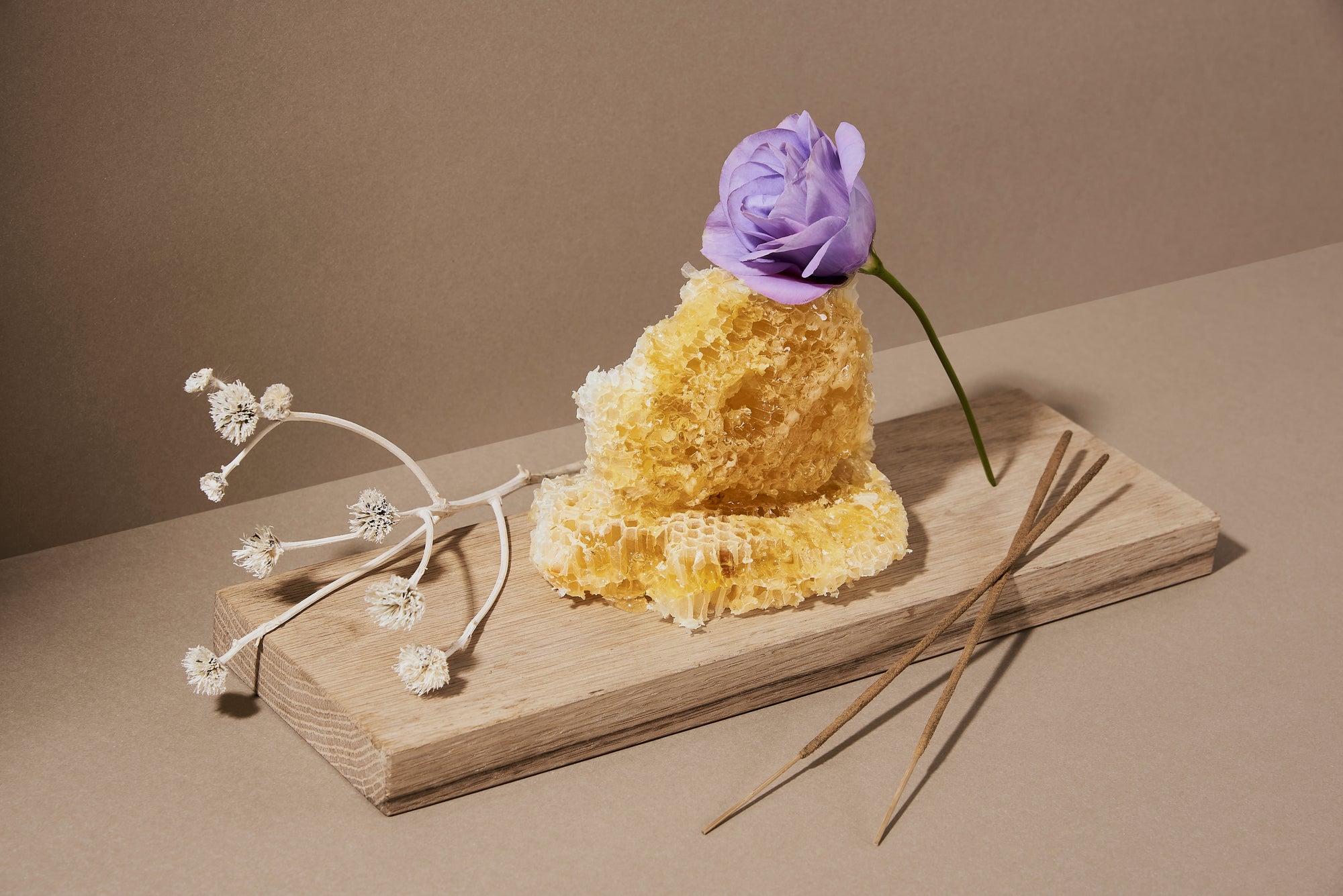 incense sticks, honeycomb and rose flower placed on a wooden plank. This is a image to describe natural ingredients used in making the hand-rolled incense sticks.