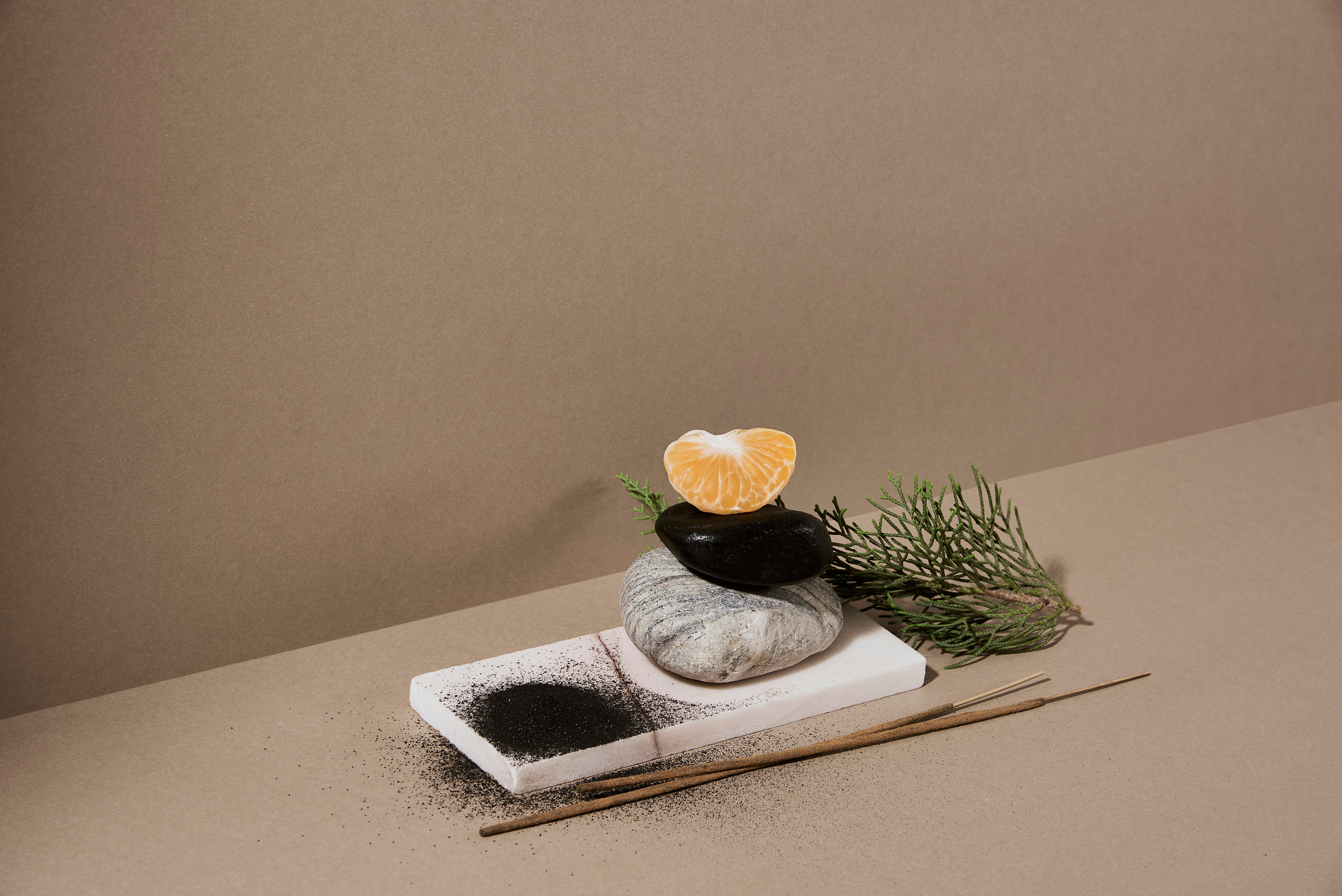 coconut husk powder, incense sticks, stones, orange and herbs on a white wooden plank. This is a pictorial description of the ingredients used in making this hand-rolled incense sticks. 